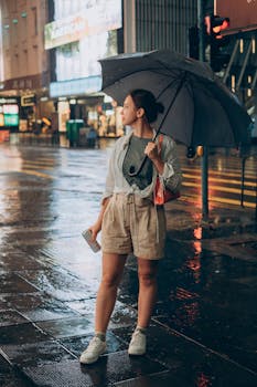 Woman standing on wet urban street with umbrella in rainy Hong Kong night.
