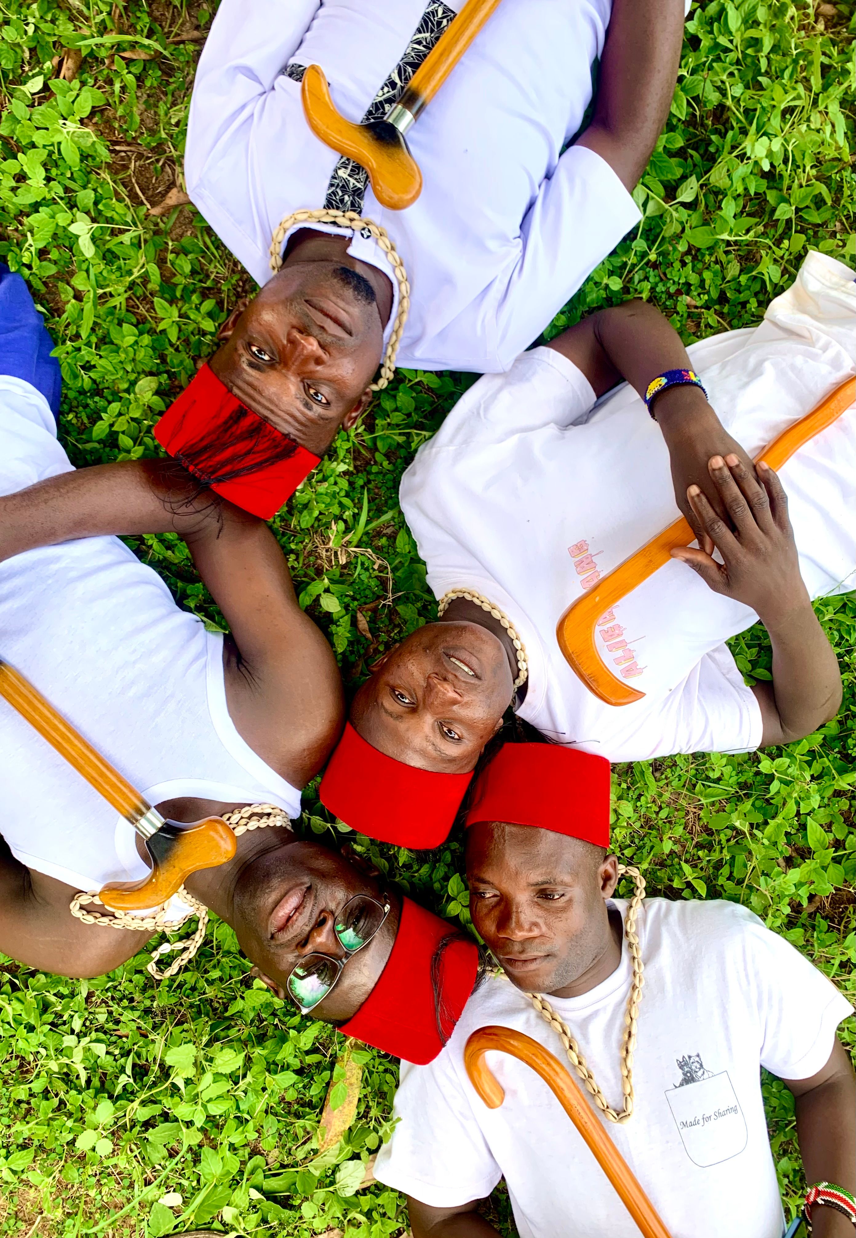 Four men wearing traditional red hats and white shirts lying on grass in a circle.