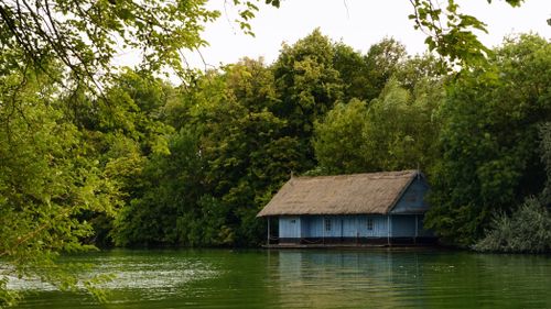 Free A serene lakeside bungalow by lush green trees, perfect for rural summer escapes. Stock Photo