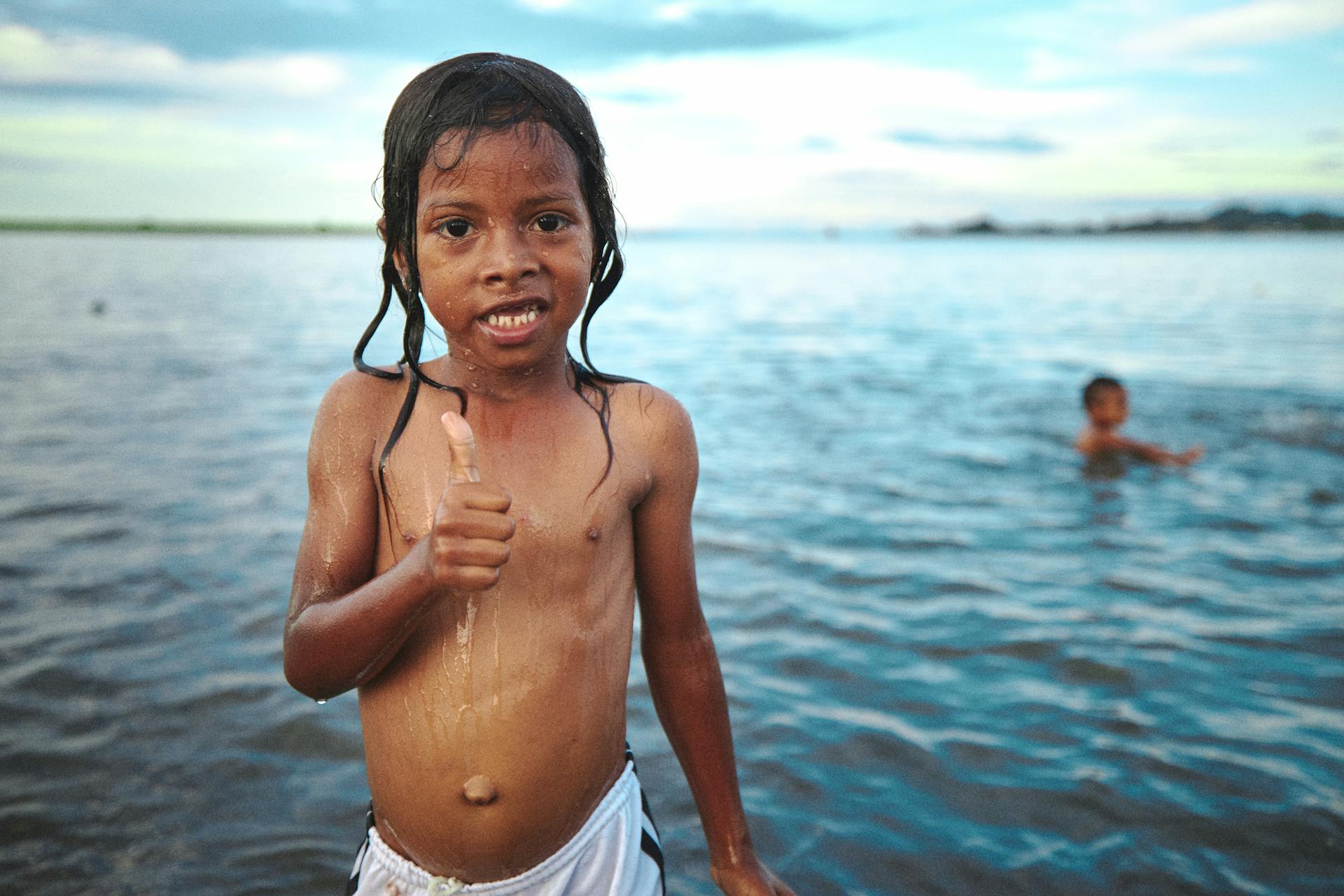 Young boy in a Colombian beach enjoying the water and giving a thumbs-up.