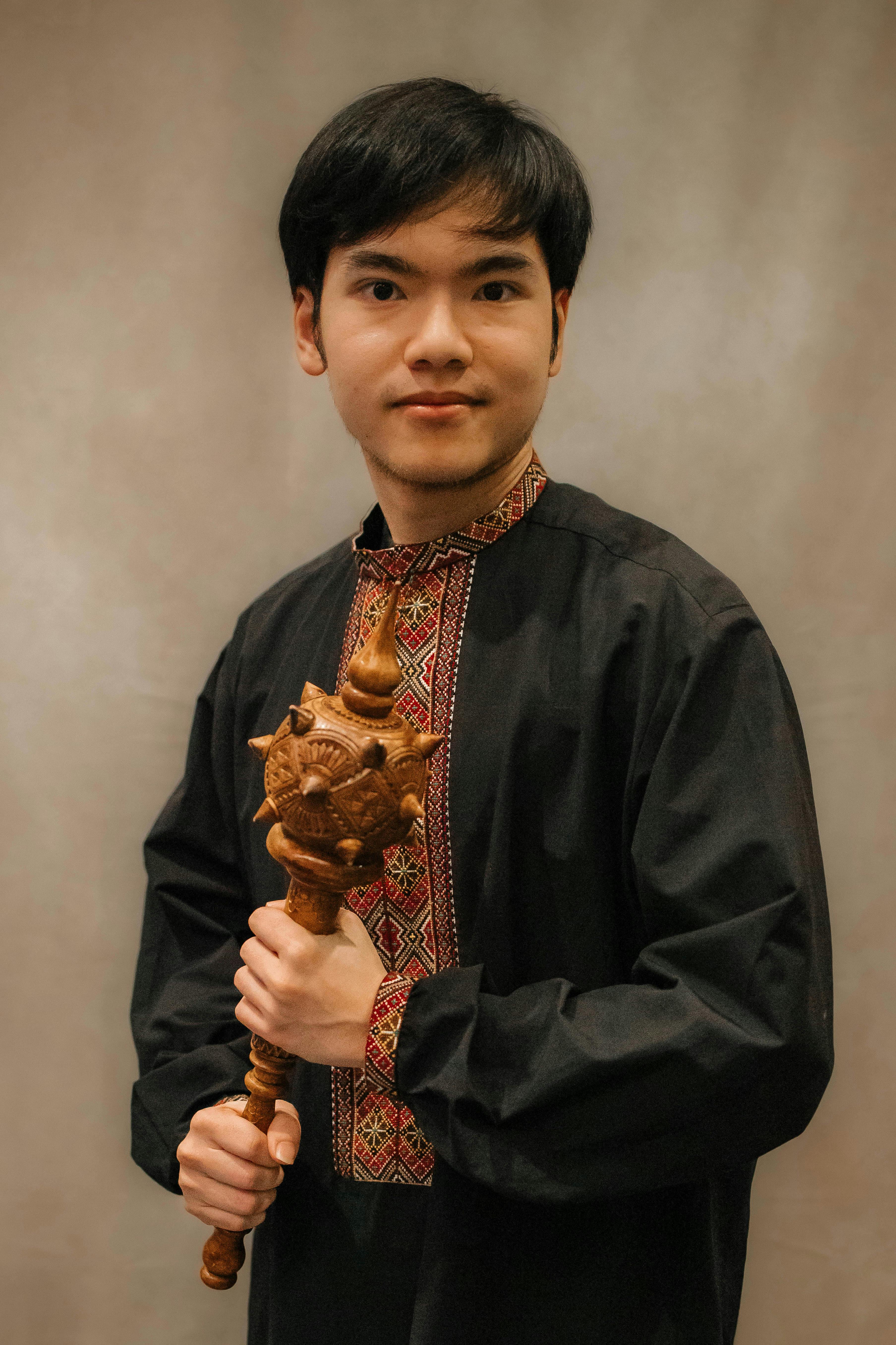 A young adult male holding a wooden tribal scepter in a traditional outfit.