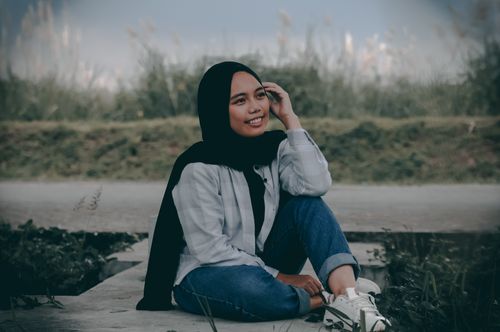 Free Young woman in hijab sitting outdoors, smiling confidently in natural setting. Stock Photo