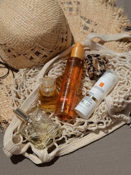 Stylish flat lay of beach bag essentials including a straw hat, sunscreen, and perfume for summer relaxation.
