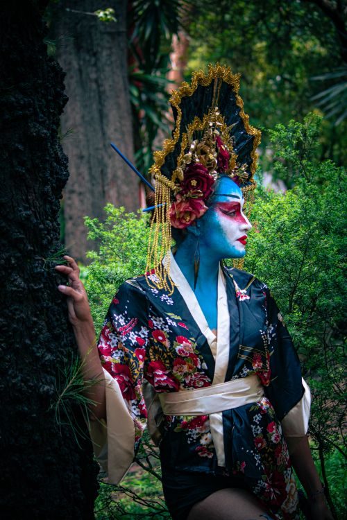 Free Vivid artistic portrait showcasing traditional geisha costume with creative makeup in a lush outdoor setting. Stock Photo