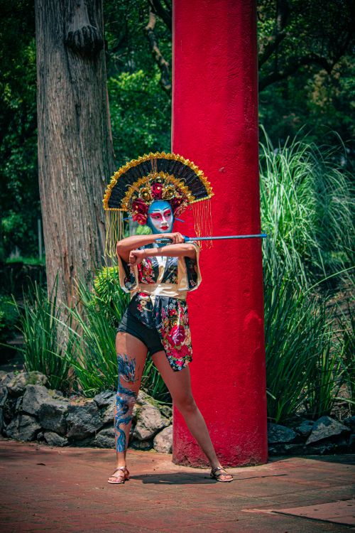 Free Striking portrait of a geisha-inspired model in an outdoor park setting, showcasing vivid makeup and traditional attire. Stock Photo
