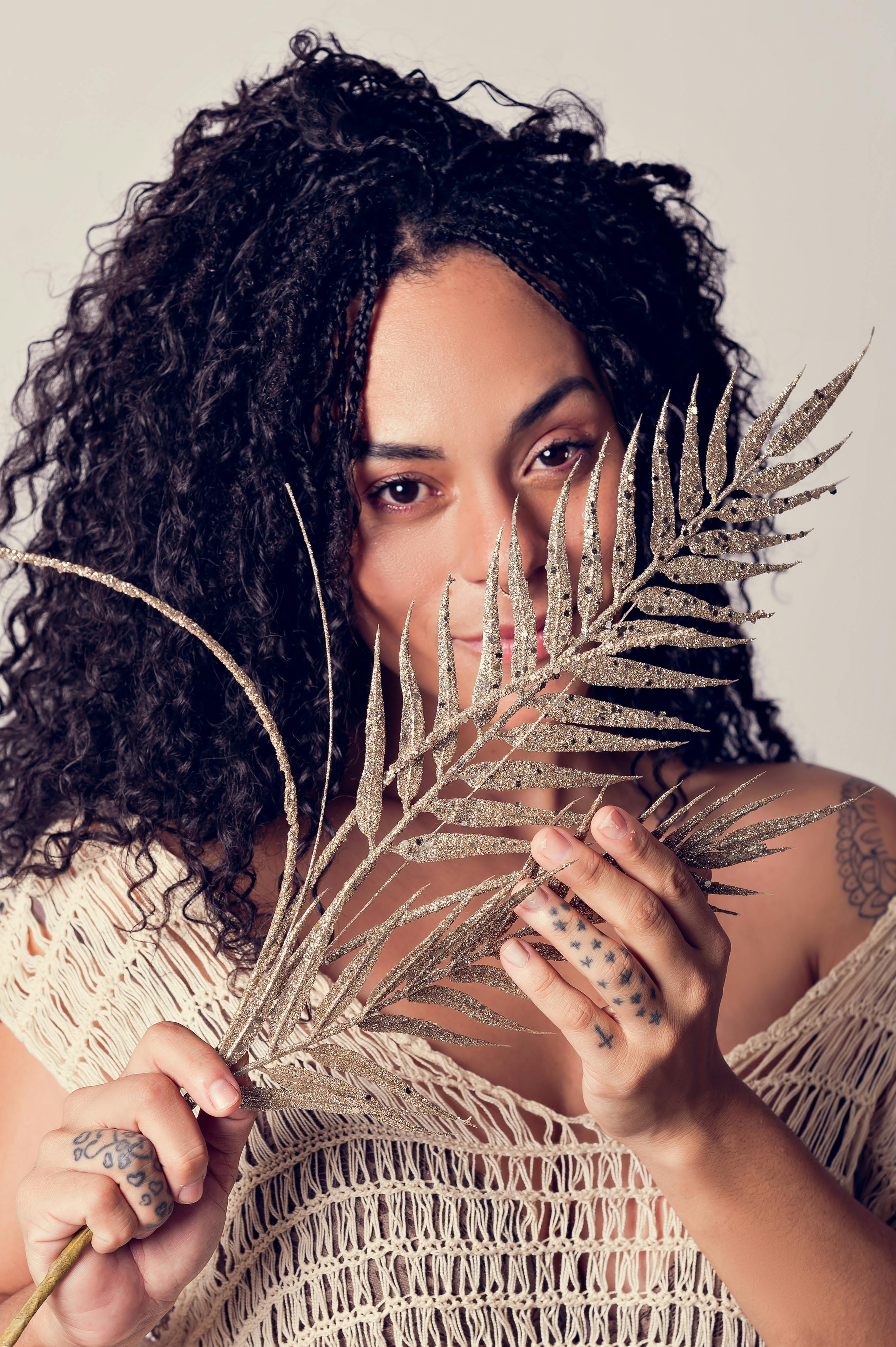Elegant portrait of a young woman holding a glittering fern leaf close to her face, exuding glamour and style.