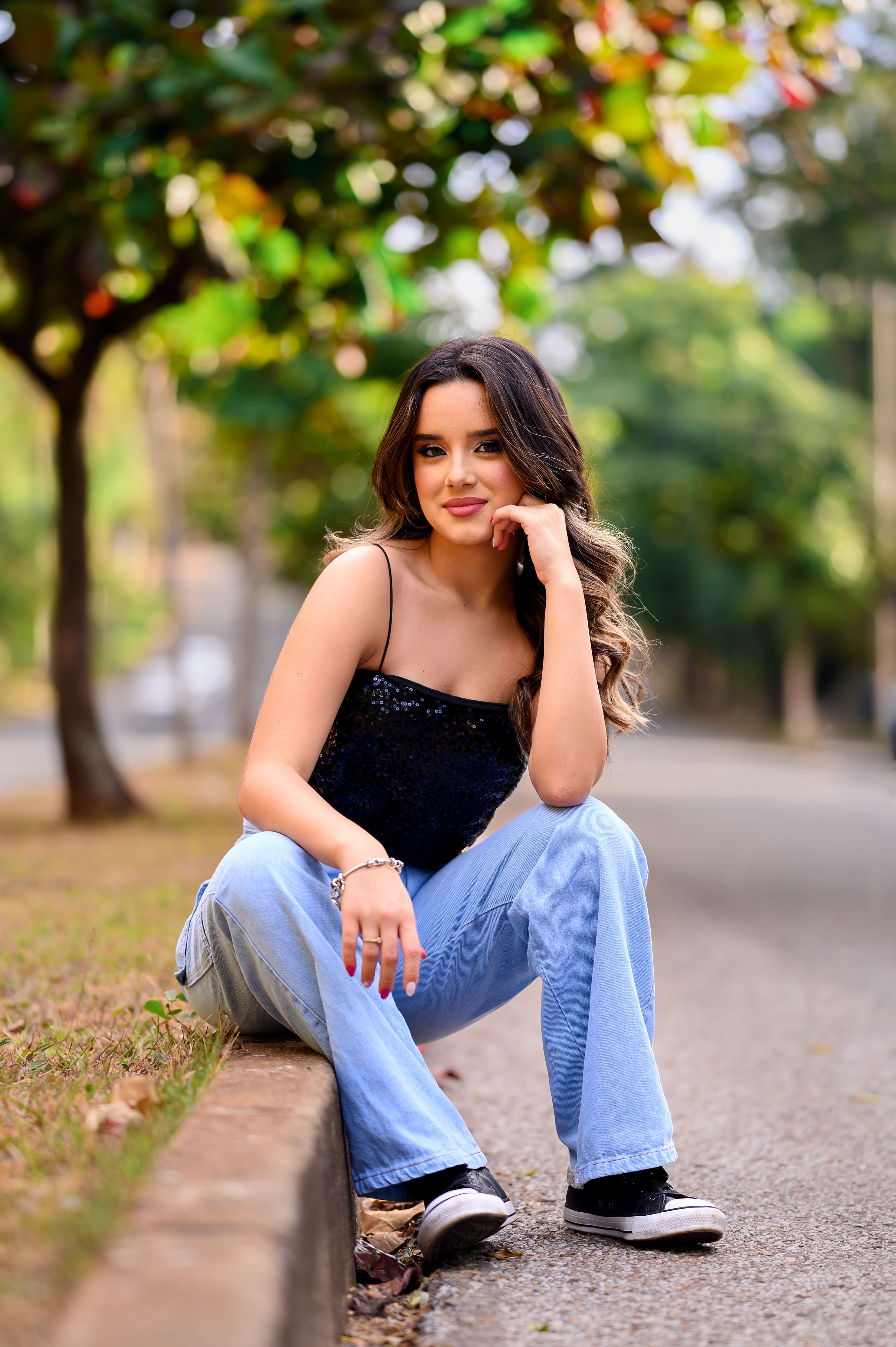 Charming young woman sitting by a park pathway, enjoying a sunny summer day.