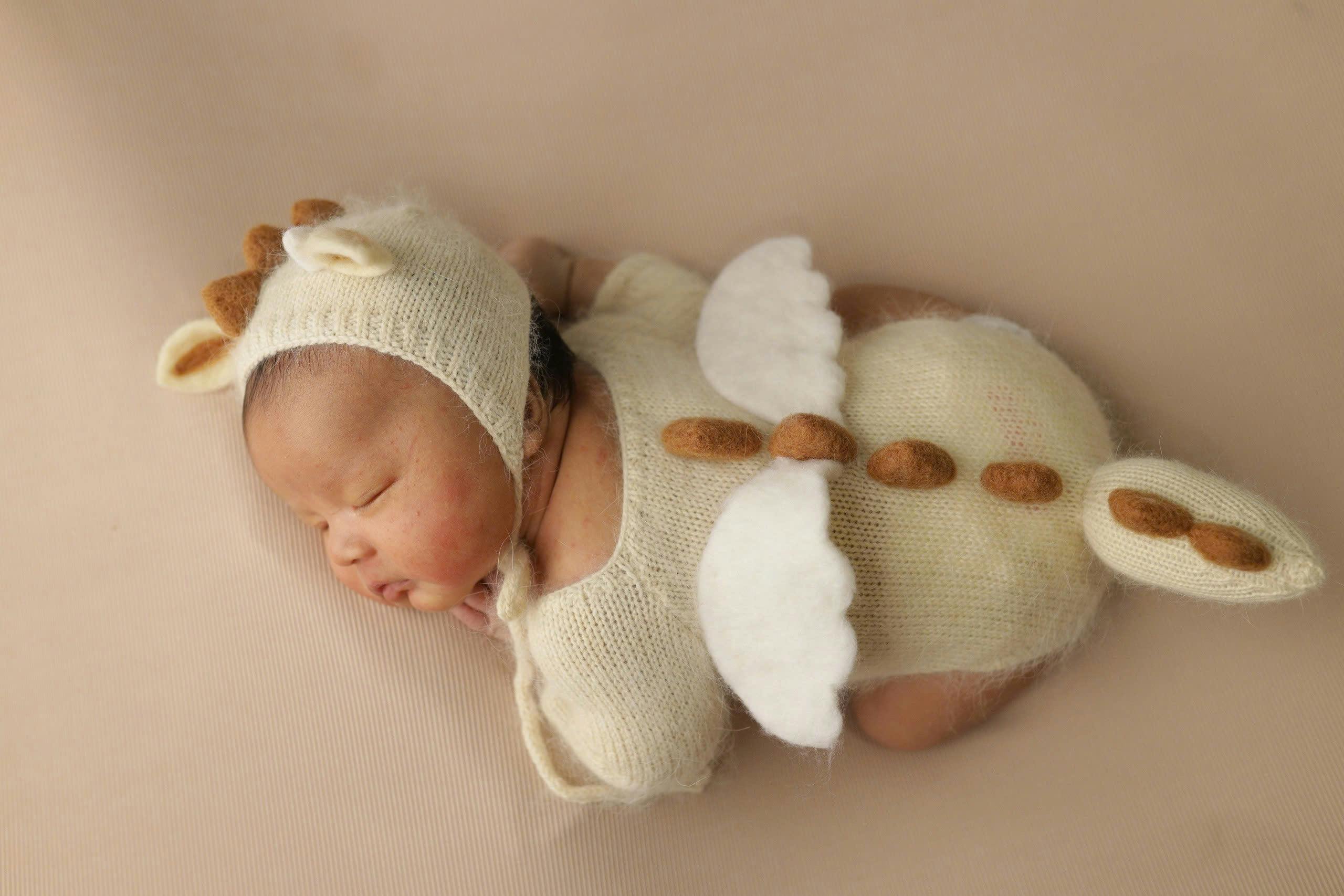 Adorable newborn baby dressed in a soft dinosaur outfit sleeping peacefully.