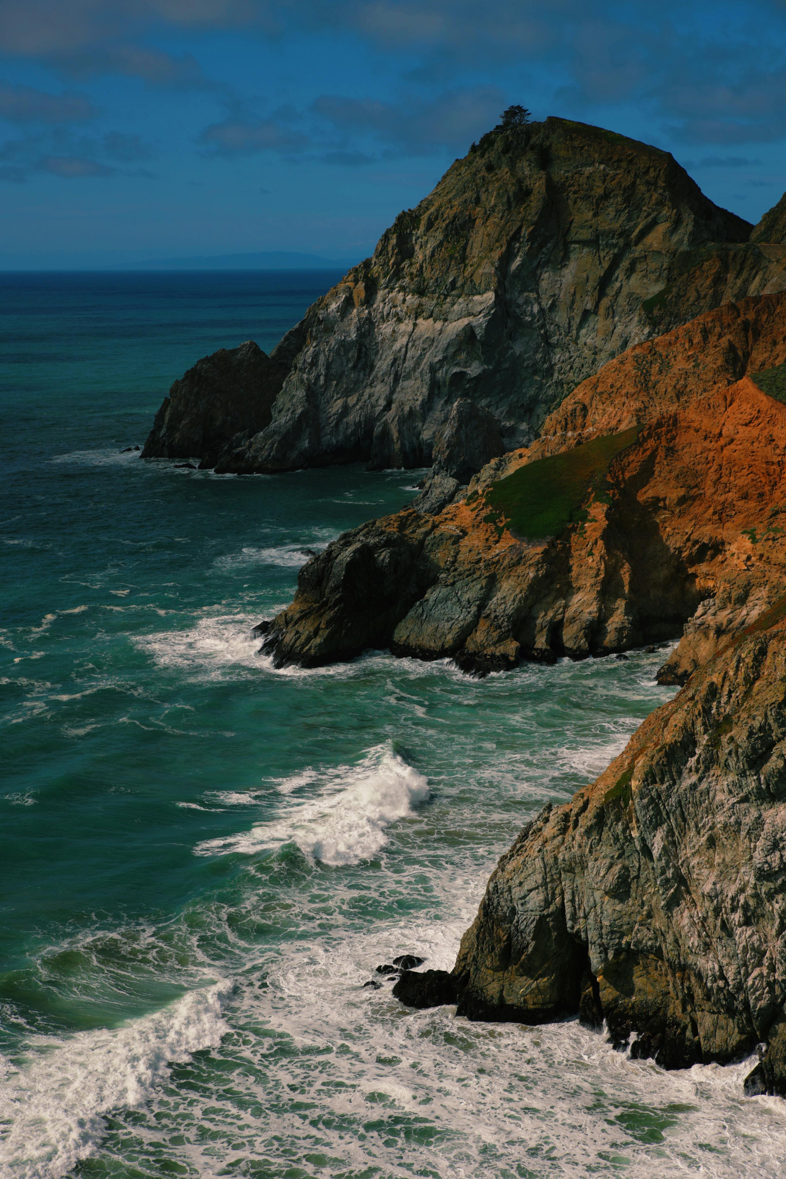 A stunning view of rocky cliffs with waves crashing along the coastline, under a bright summer sky.