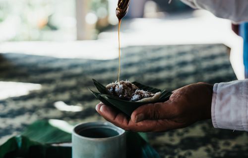 Free A hand holding traditional food with sauce drizzle over banana leaf captured outdoors. Stock Photo