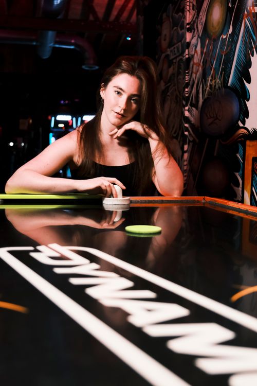 Free A woman engaged in an exciting air hockey match at a vibrant arcade space, capturing the nightlife fun. Stock Photo