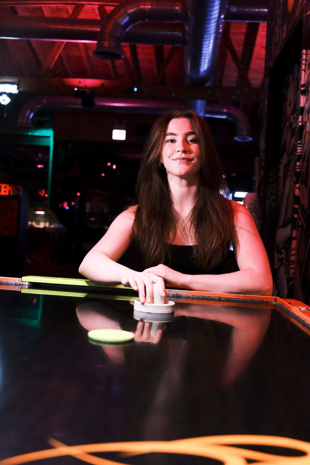 A woman enjoys a game of air hockey in a dimly lit nightclub setting. Stock Photo.