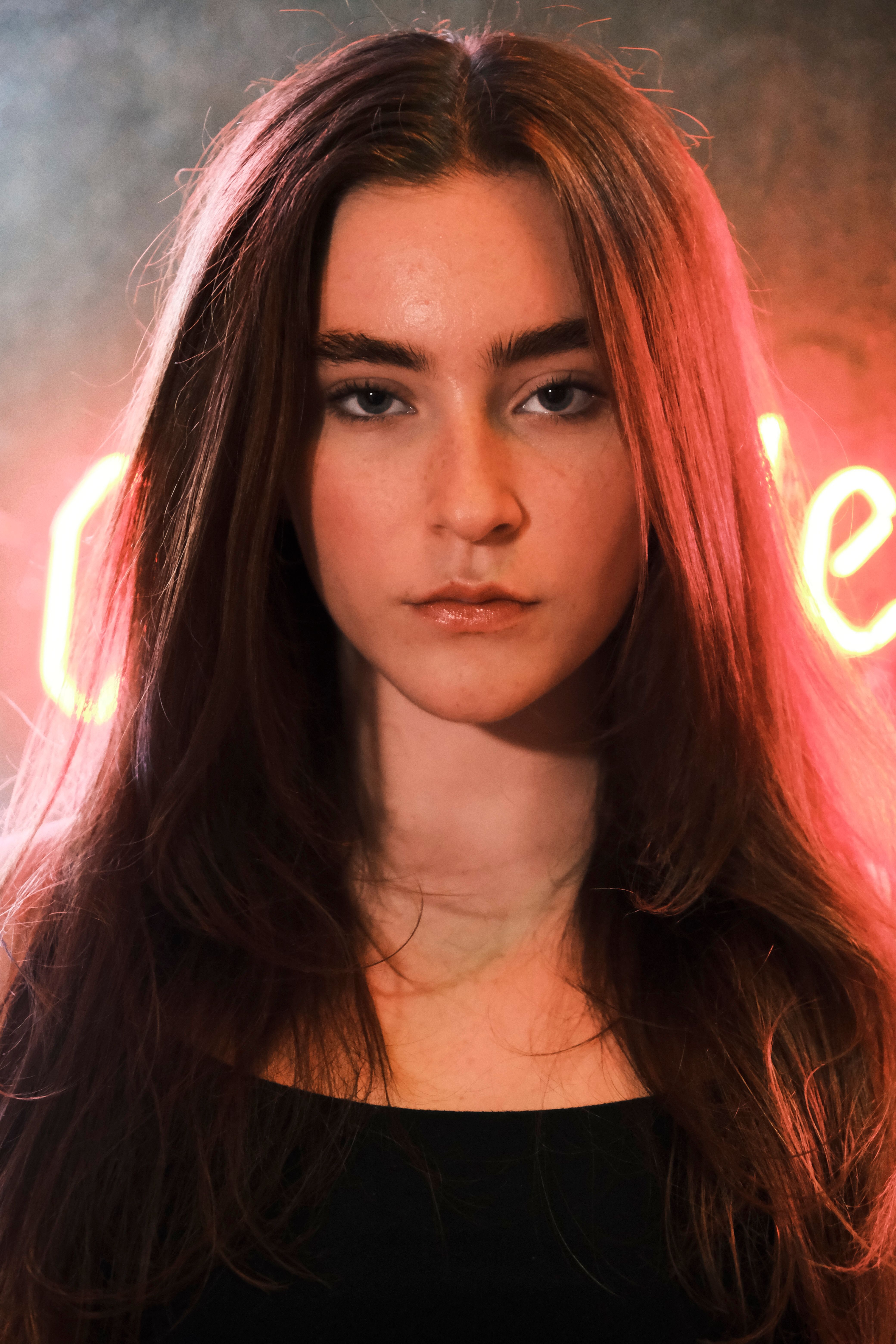 Portrait of a young woman with long auburn hair, illuminated by neon lighting, exuding elegance and confidence.