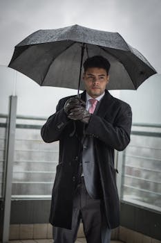 Stylish businessman in a suit holding an umbrella on a rainy day outdoors.