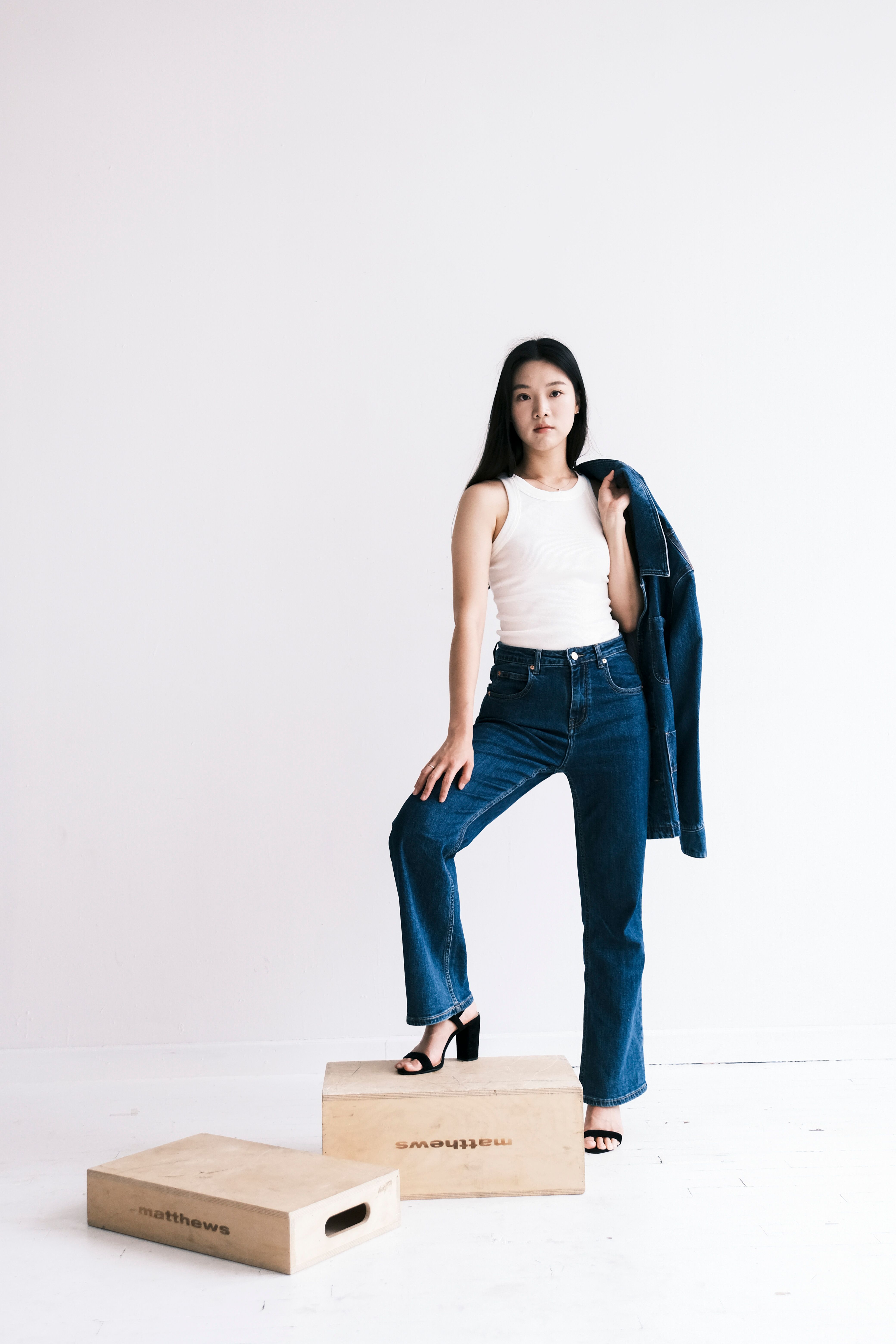 Young woman in stylish denim outfit posing confidently against a minimalist white background.