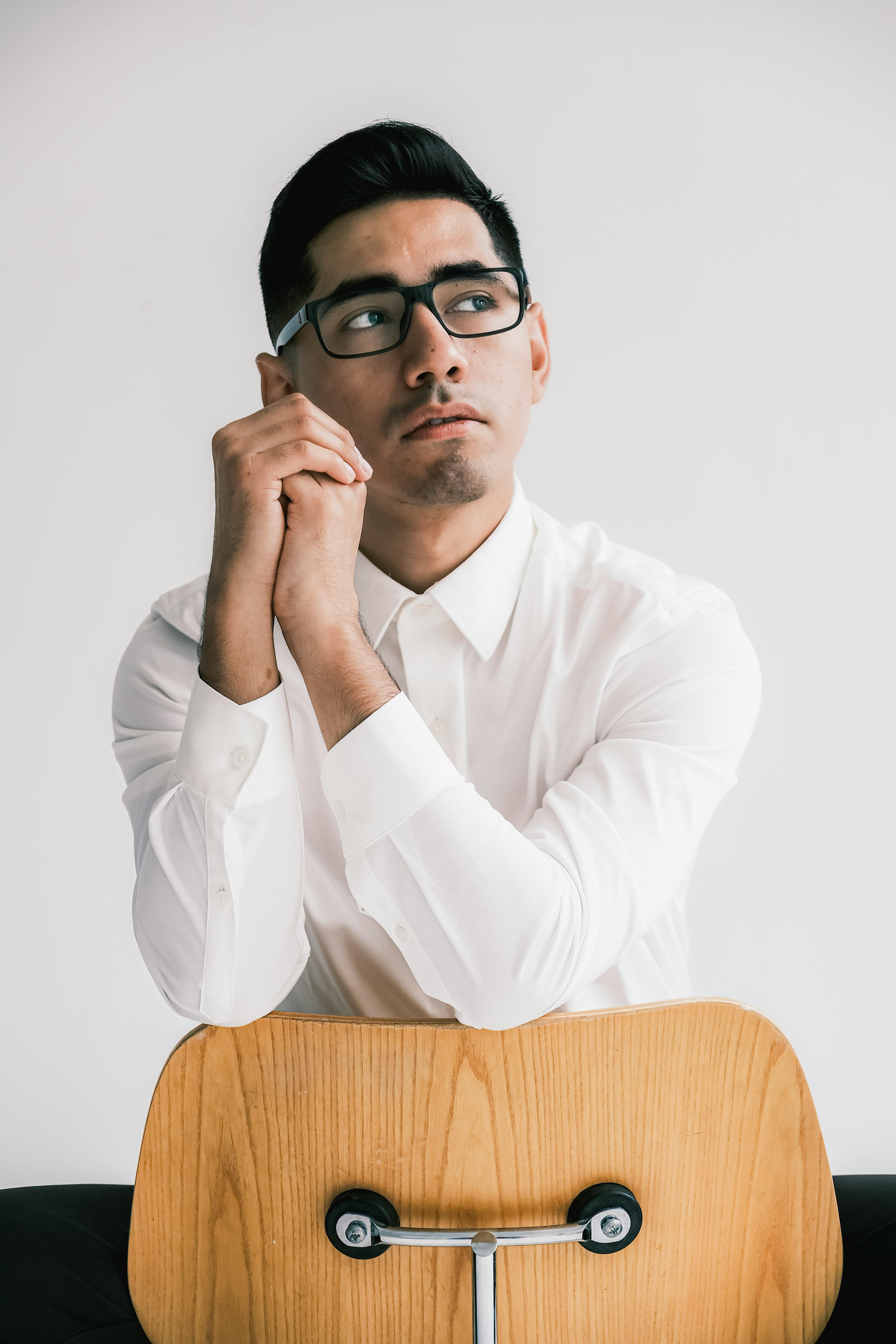 Portrait of a man wearing glasses and a white shirt, seated backward on a chair in a studio.