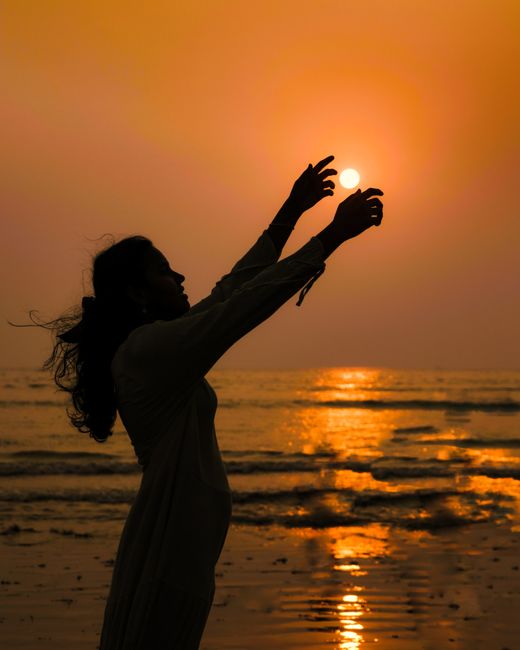 A serene silhouette of a woman reaching towards the sun during a captivating sunset on a Mumbai beach.