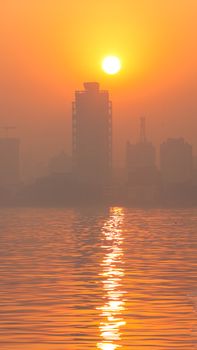 Golden sunset over Mumbai skyline with reflection on water, creating a serene atmosphere.