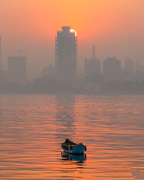 Free Serene view of Mumbai skyline with a boat on calm waters during sunset. Stock Photo
