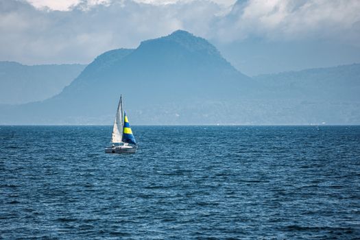 A sailboat glides on a serene lake against a misty mountain backdrop, perfect for nature and travel themes.
