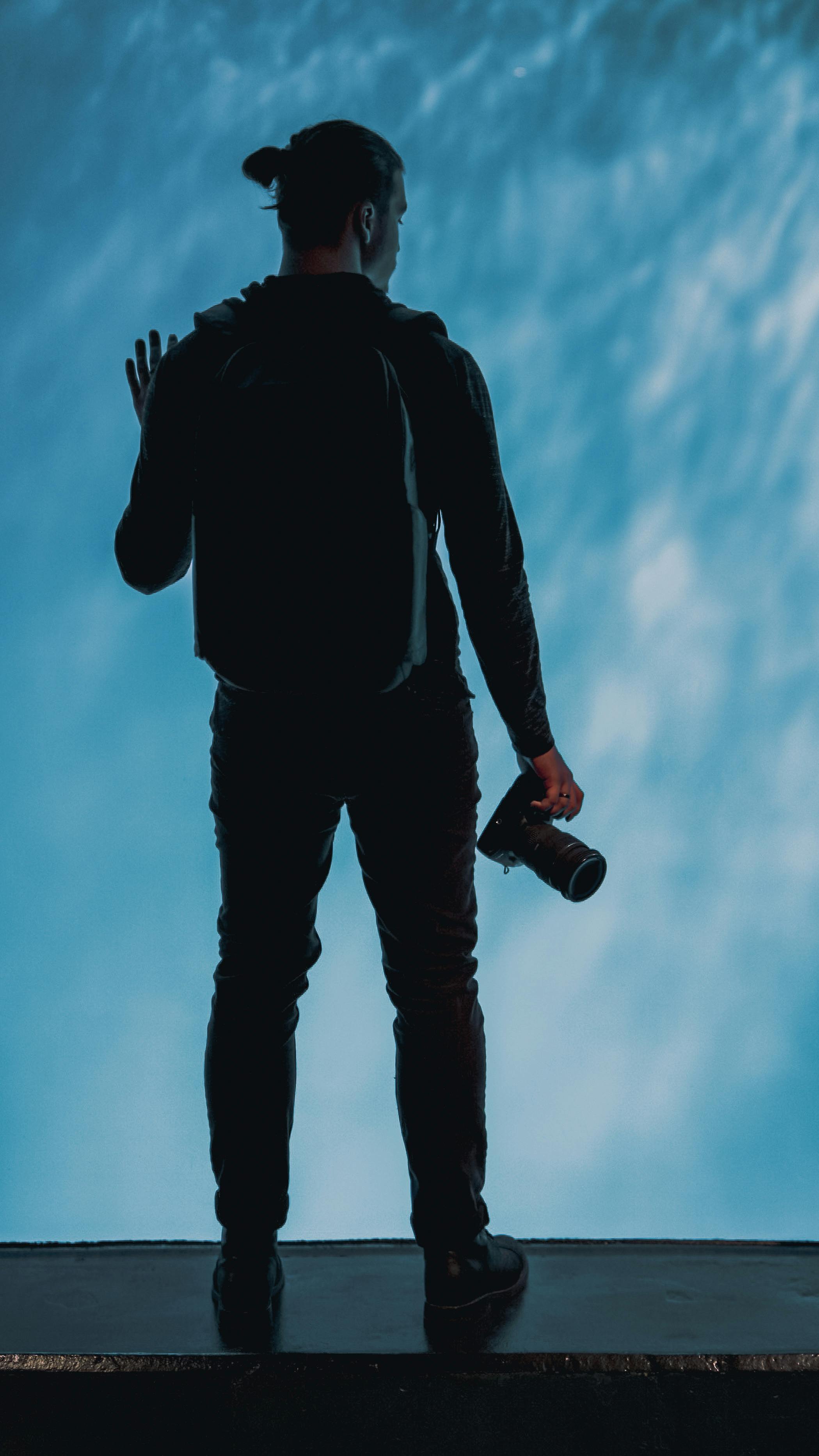Silhouette of a photographer holding a DSLR camera against a bright blue aquatic backdrop.