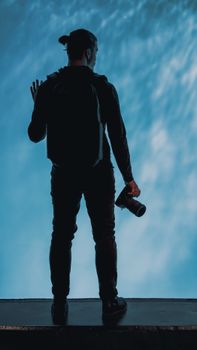 Silhouette of a photographer holding a DSLR camera against a bright blue aquatic backdrop.