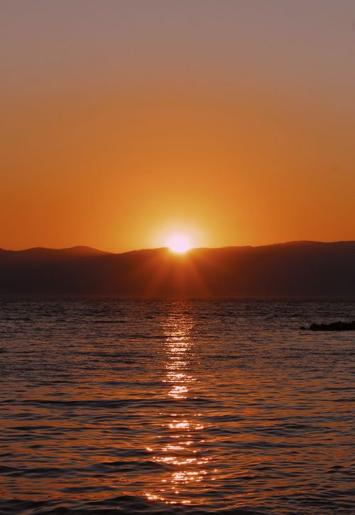 Free Serene sunset with vibrant orange tones reflecting on the calm ocean waters. Stock Photo