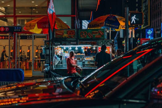 Urban night scene showcasing a bustling food cart near Times Square subway entrance.