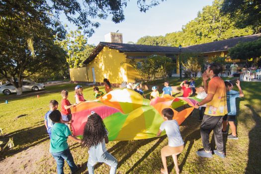 Group of children playing with a colorful parachute outside during a sunny day party.