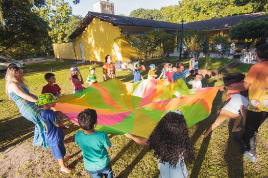 A lively group of children joyfully playing with a colorful parachute at an outdoor summer gathering.