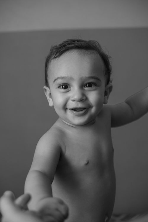 Free Black and white portrait of a smiling baby reaching out indoors. Stock Photo