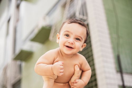 Free A baby exudes happiness with a bright smile while being lifted outdoors on a sunny day. Stock Photo