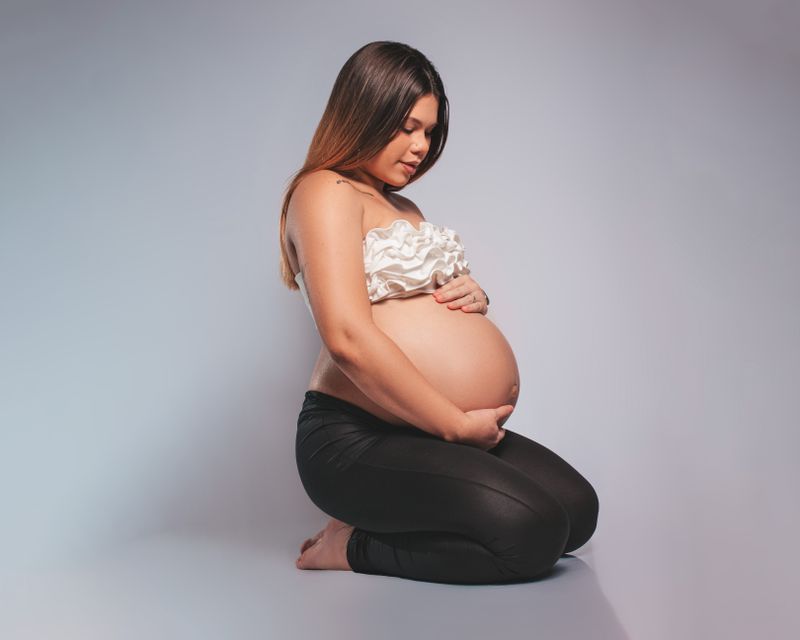 Portrait of a pregnant woman kneeling, showcasing maternity elegance and anticipation in a studio setting.