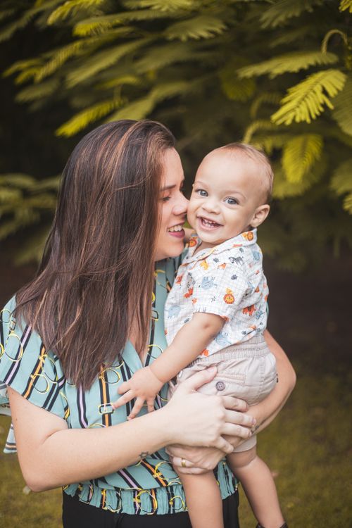 Free A heartwarming moment between a smiling mother and her baby outdoors with lush greenery. Stock Photo