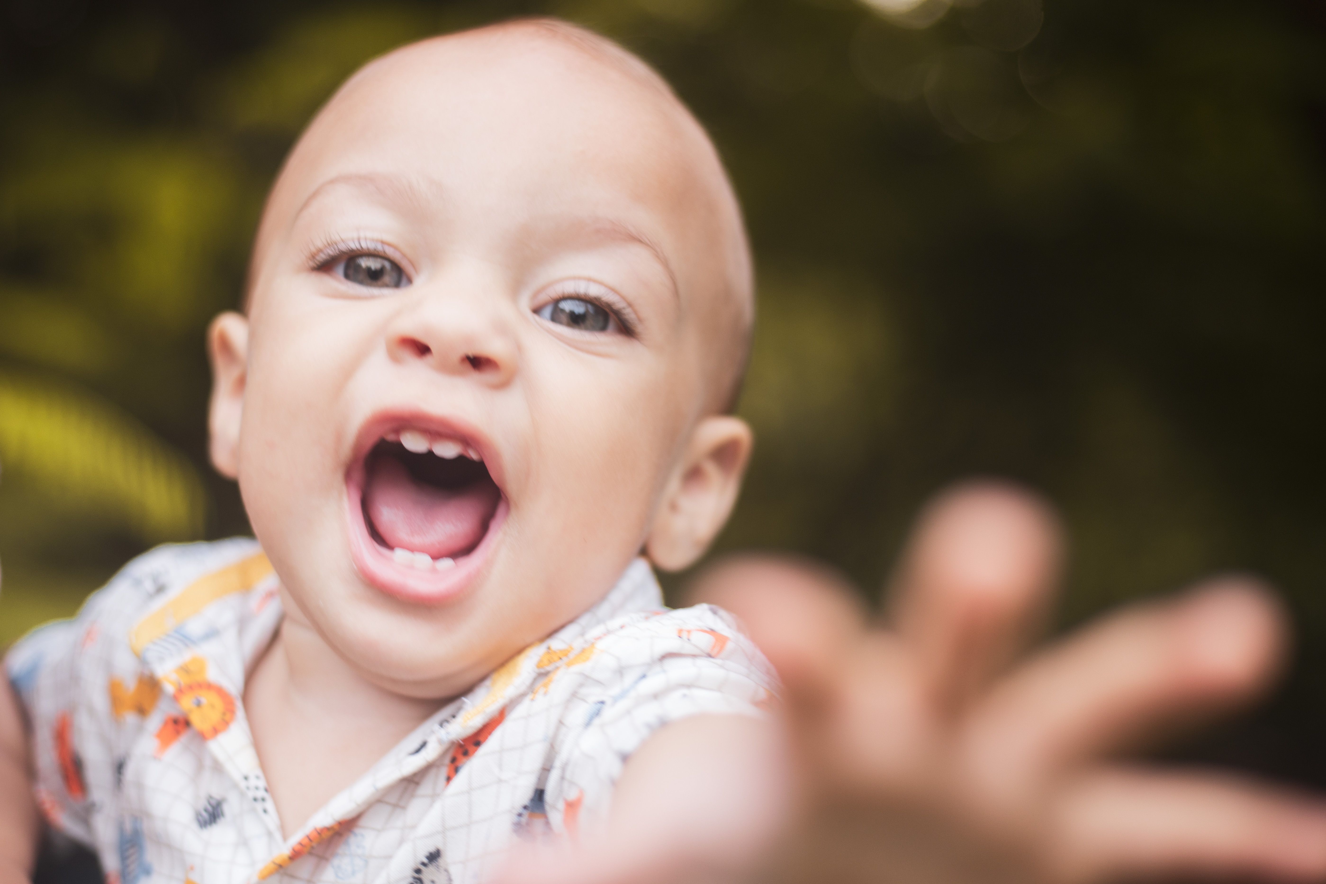 Close-up of a happy baby reaching out with a joyful expression outdoors.