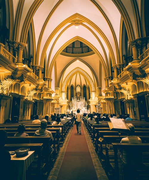 Free A stunning interior view of a Gothic church with vaulted ceilings and people attending a service. Stock Photo