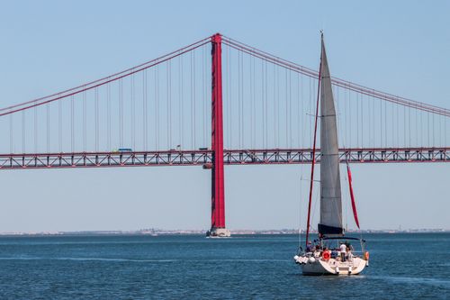 Free Sailboat under the iconic 25th of April Bridge in Lisbon, Portugal, on a clear day. Stock Photo