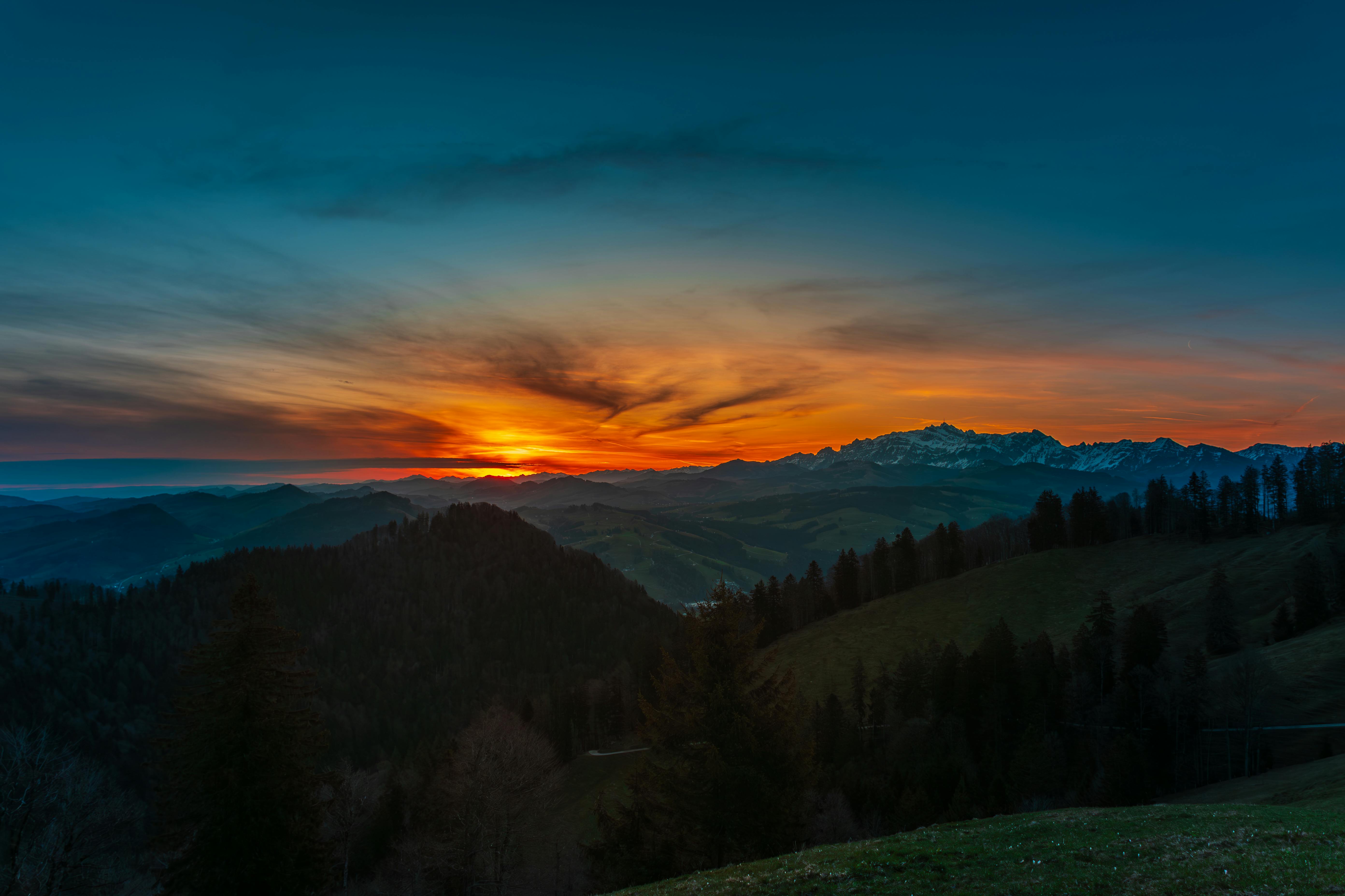 a sunset over a mountain range with trees and grass