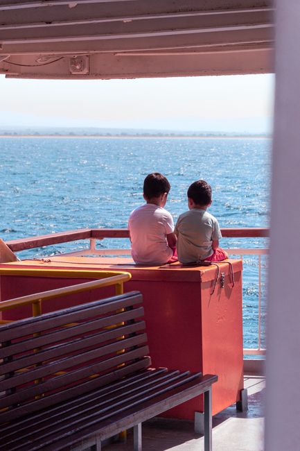 Two children sitting on a ferry enjoying a sunny day at sea.