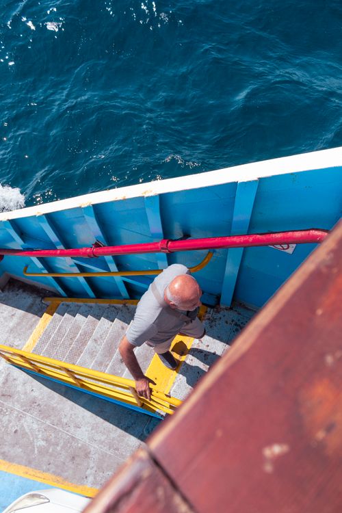 Free A man climbs the stairs of a boat with vibrant blue sea in the background, showcasing travel and adventure. Stock Photo