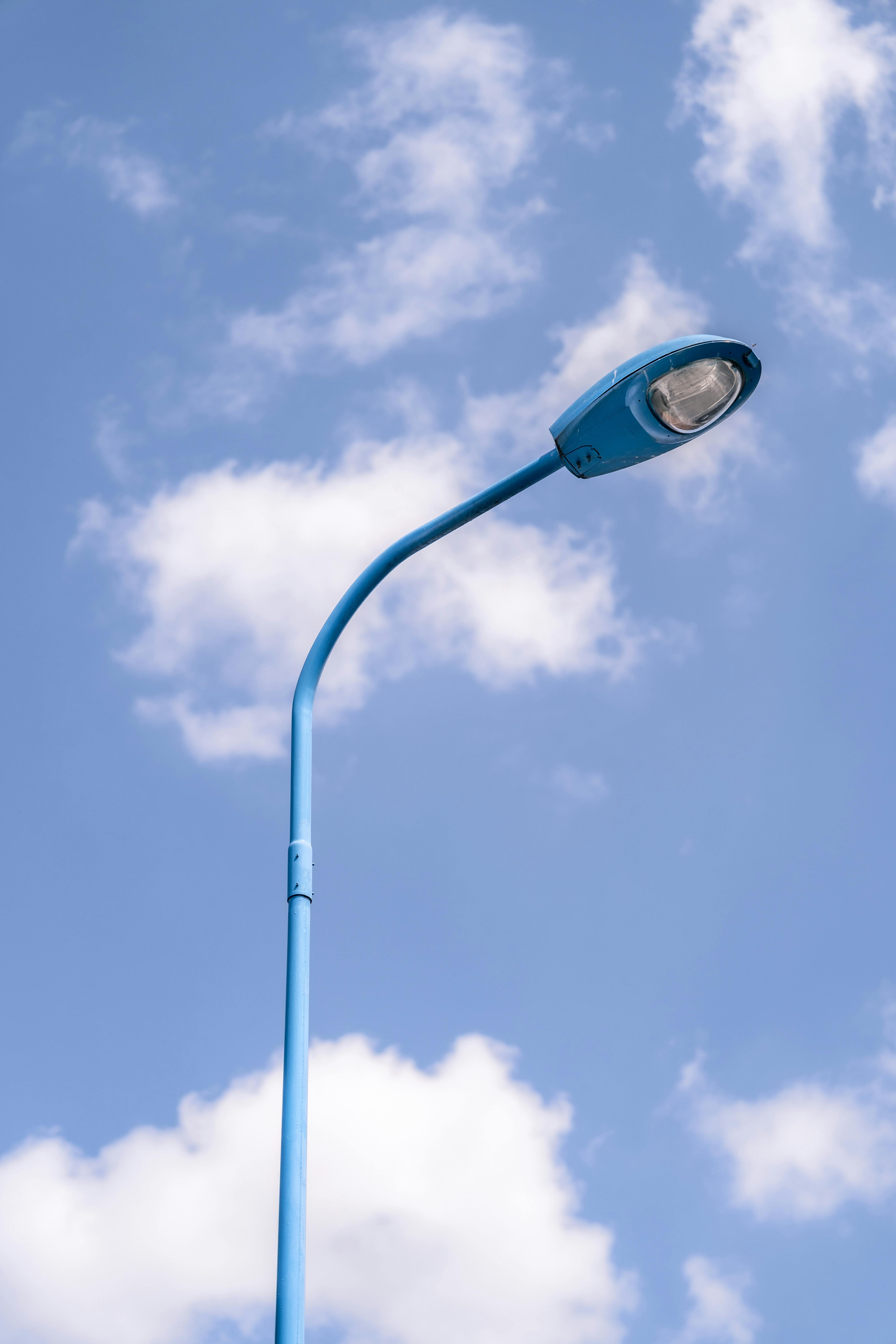 A minimalist streetlight set against a bright blue sky with scattered clouds.