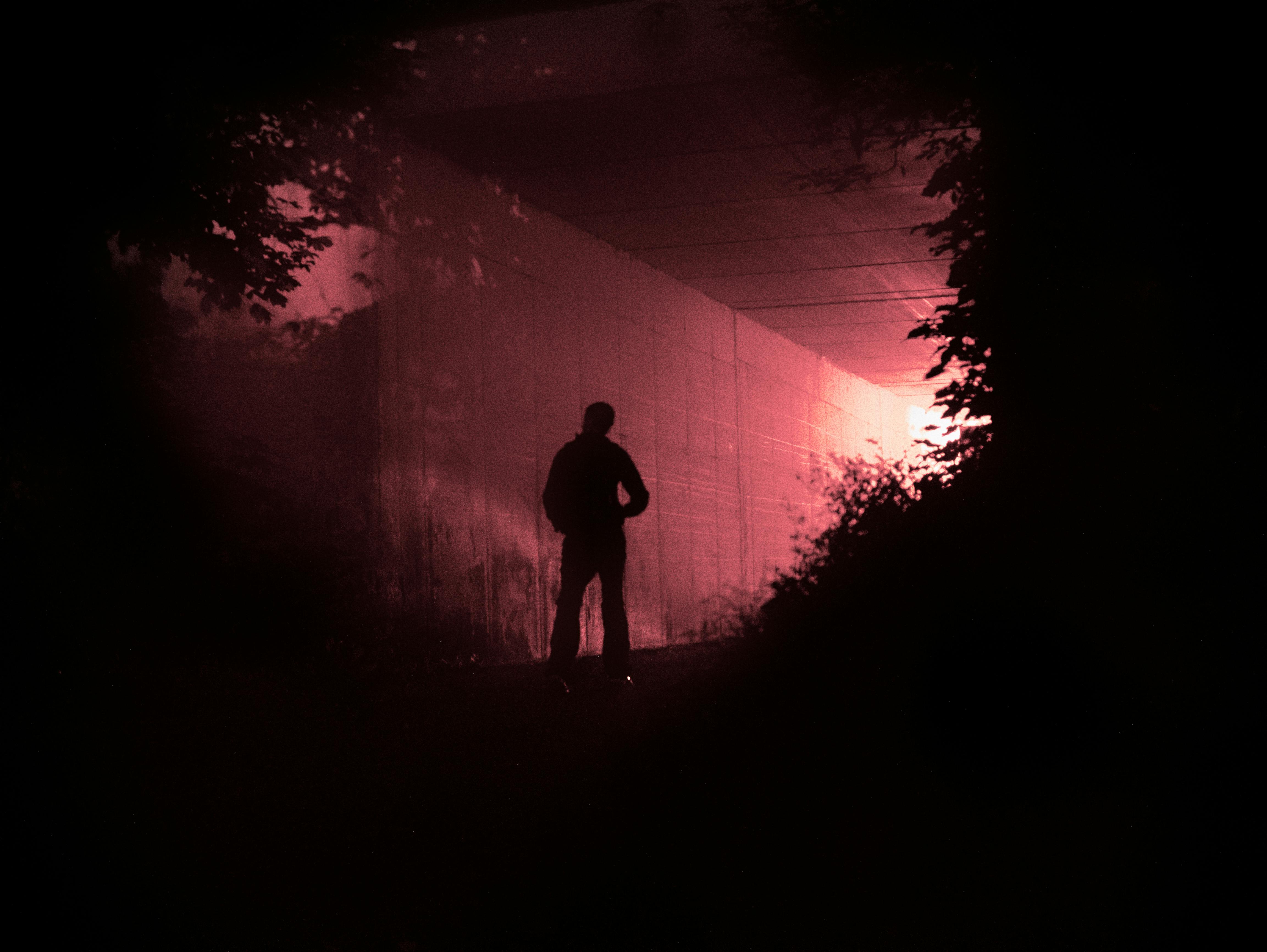 Silhouette of a person standing in a red-lit tunnel creating a dramatic and surreal atmosphere.