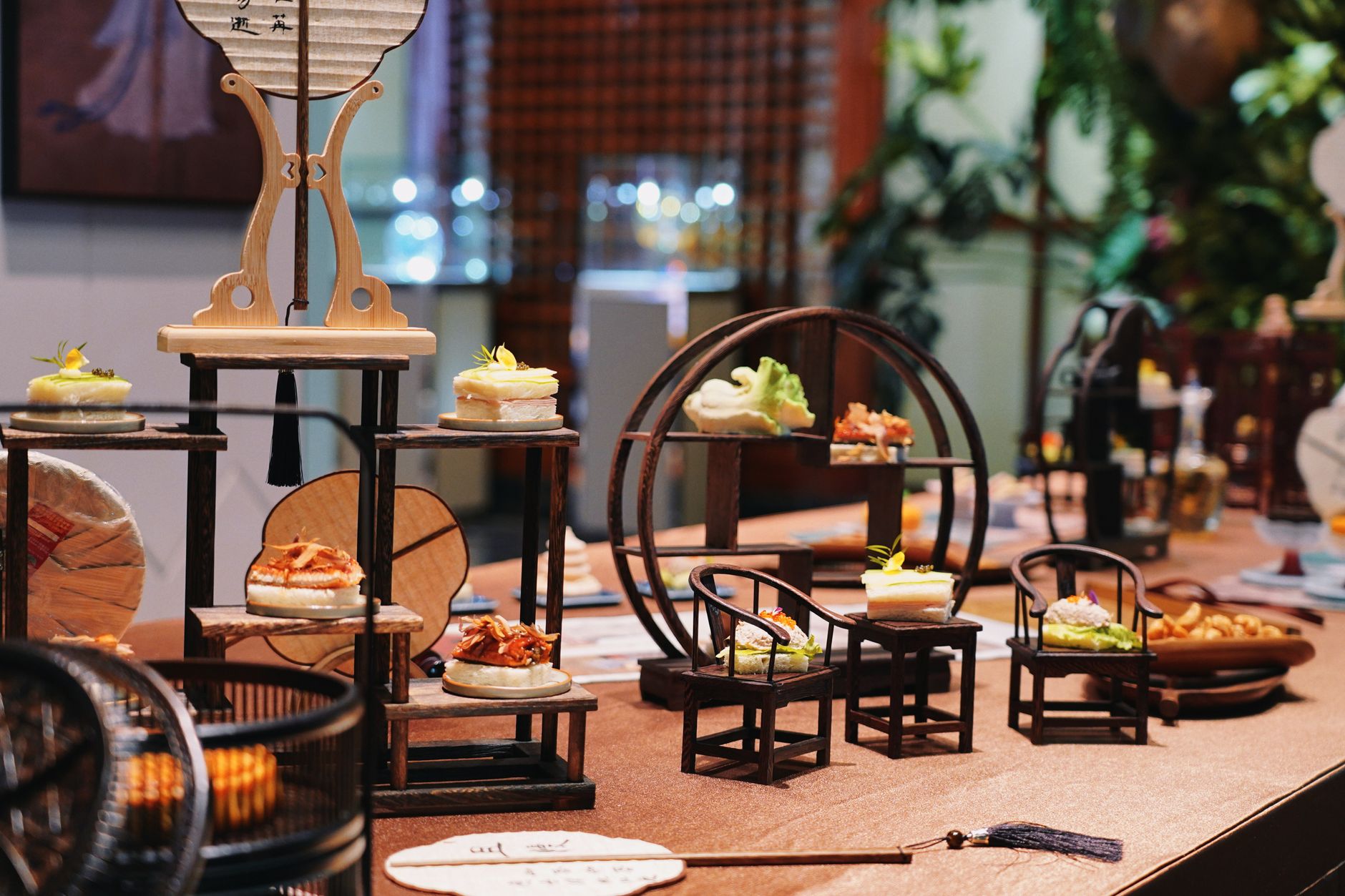 Elegant restaurant interior with luxury table settings, miniature decorative furniture, and gourmet food presentation.