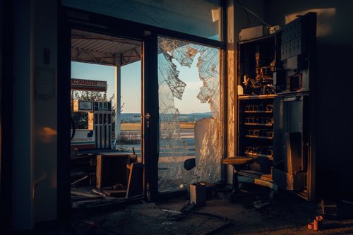 Free An indoor view of a deserted gas station featuring a shattered glass door under warm light. Stock Photo