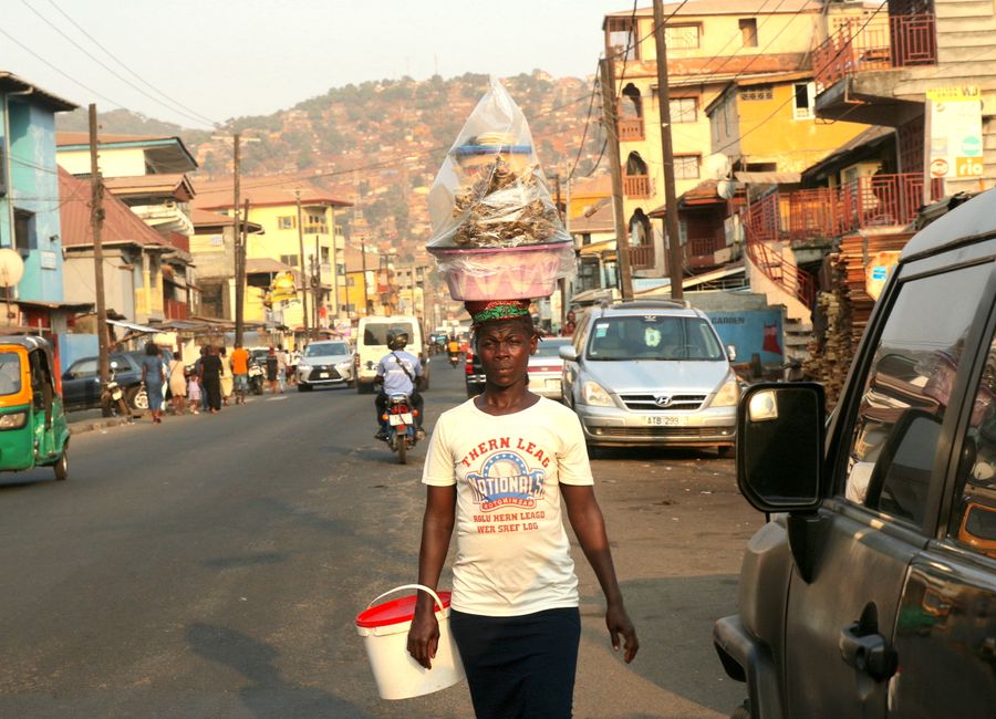 A street vendor carries goods on her head in a busy urban street of Freetown, Sierra Leone.