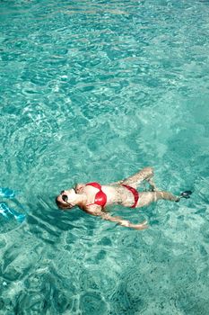 A woman in a red bikini relaxes in a tropical swimming pool, enjoying her vacation.