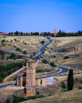 Curved road leading to a historic church in the Spanish countryside, surrounded by fields.