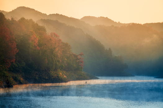 A peaceful misty morning view of a lake surrounded by autumn foliage in Cao Bằng, Vietnam.