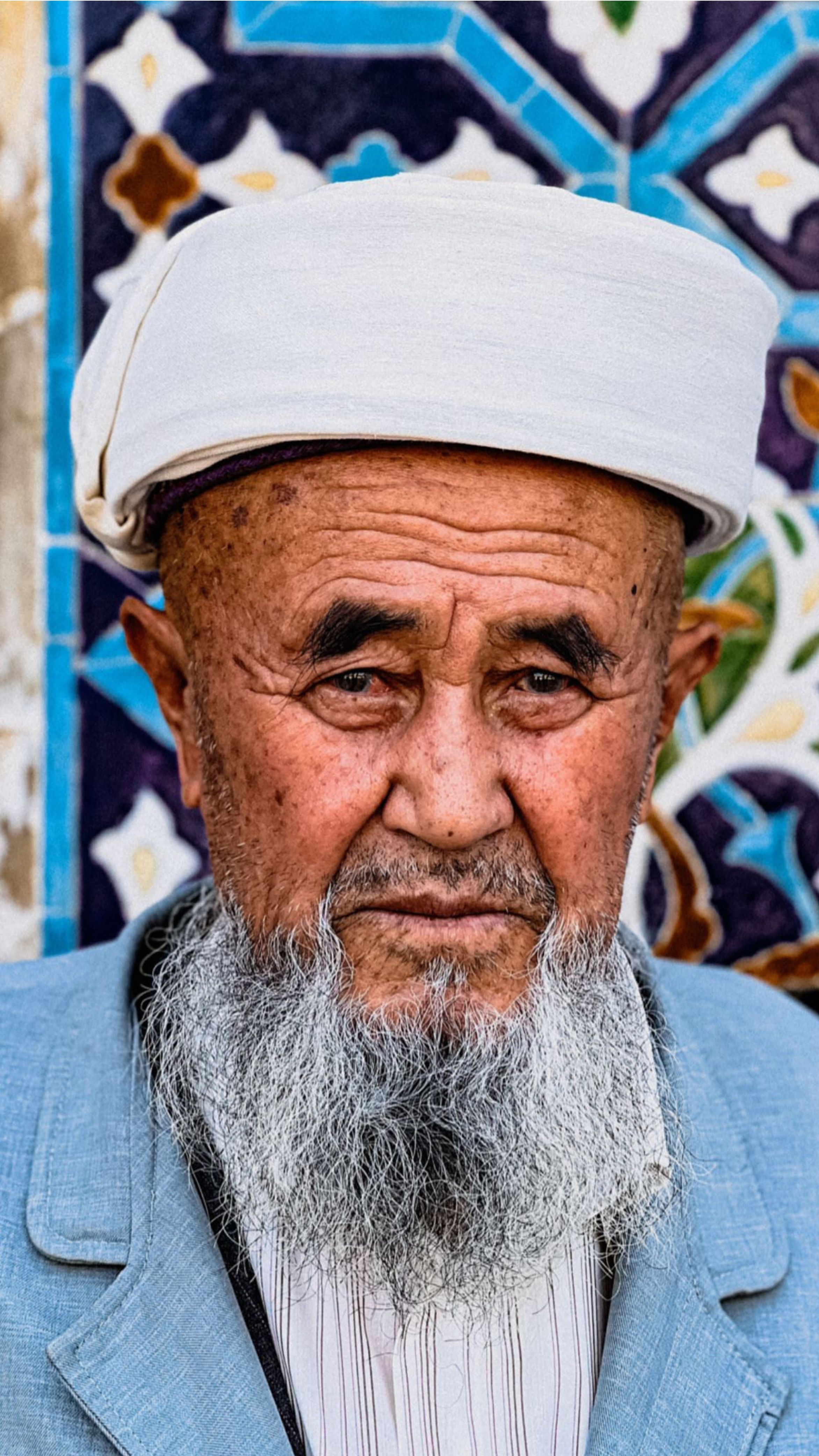 Close-up portrait of an elderly man with a traditional cap in Bukhara, Uzbekistan. Vibrant background art.