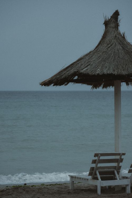 Free Tranquil beach with an empty chair under a thatched umbrella, ideal for a peaceful getaway. Stock Photo